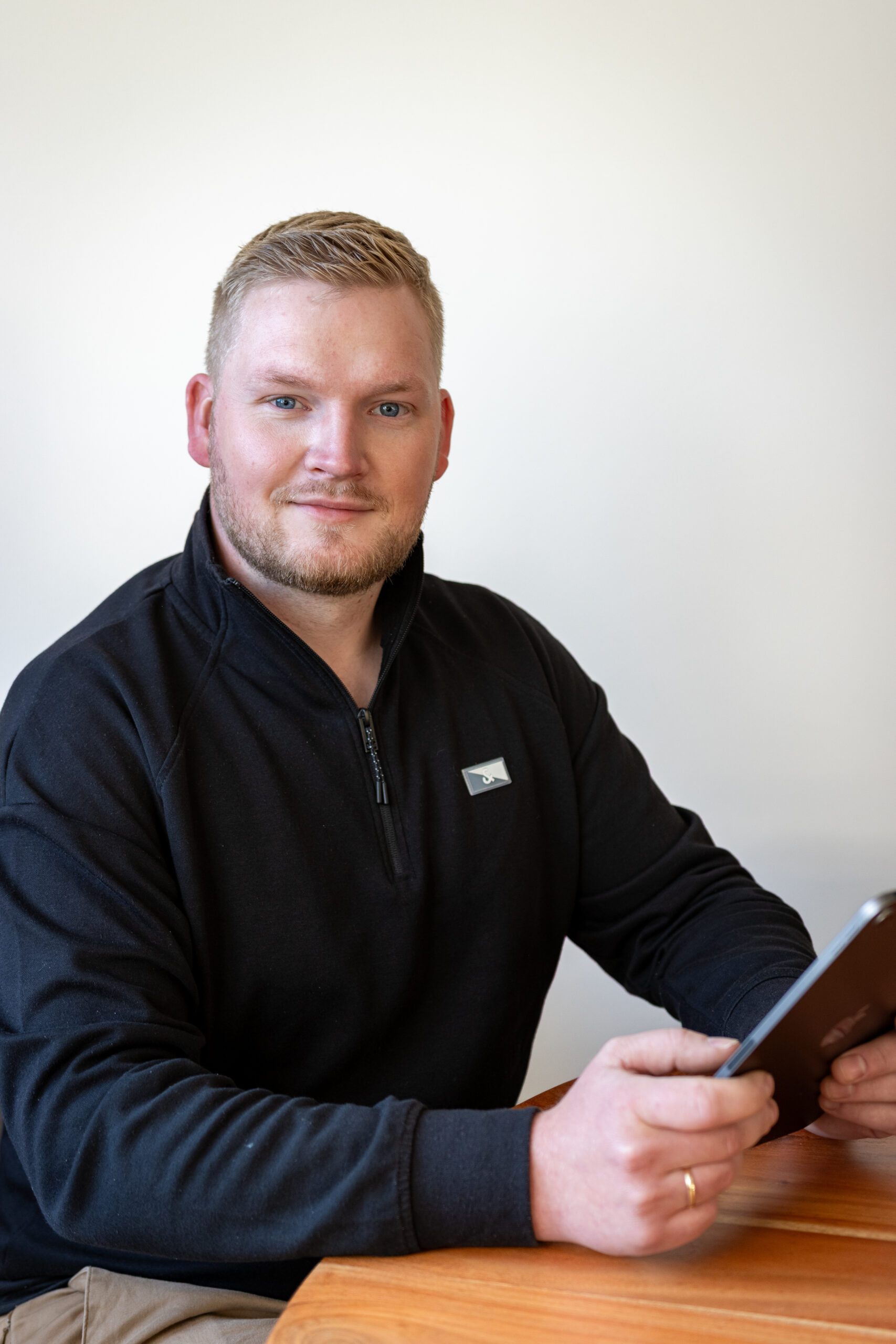Raoul Steenken sitzt an einem Holztisch mit Tablet in der Hand und schaut ruhig in die Kamera